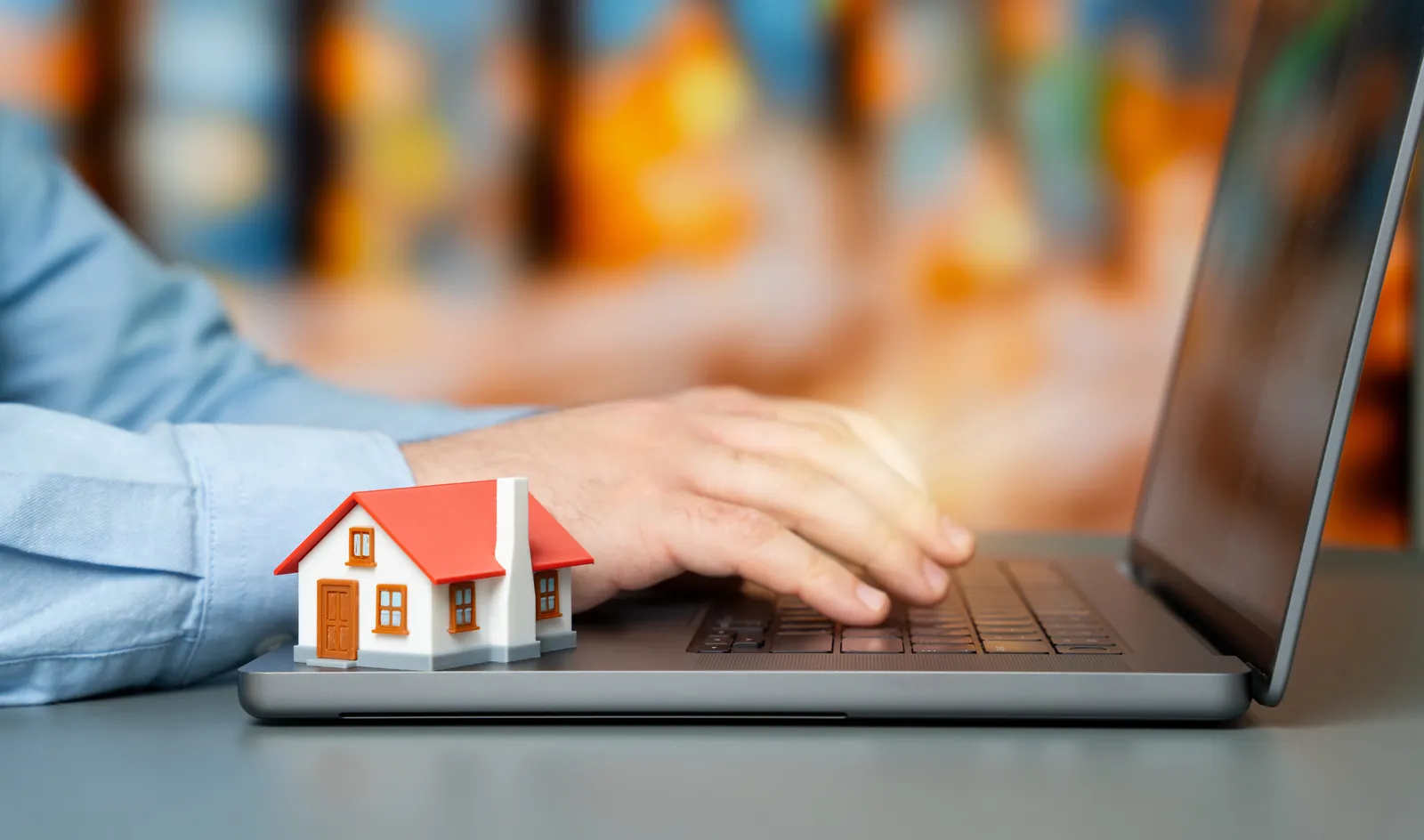 An investor browsing rental homes on a laptop with a model house beside the keyboard