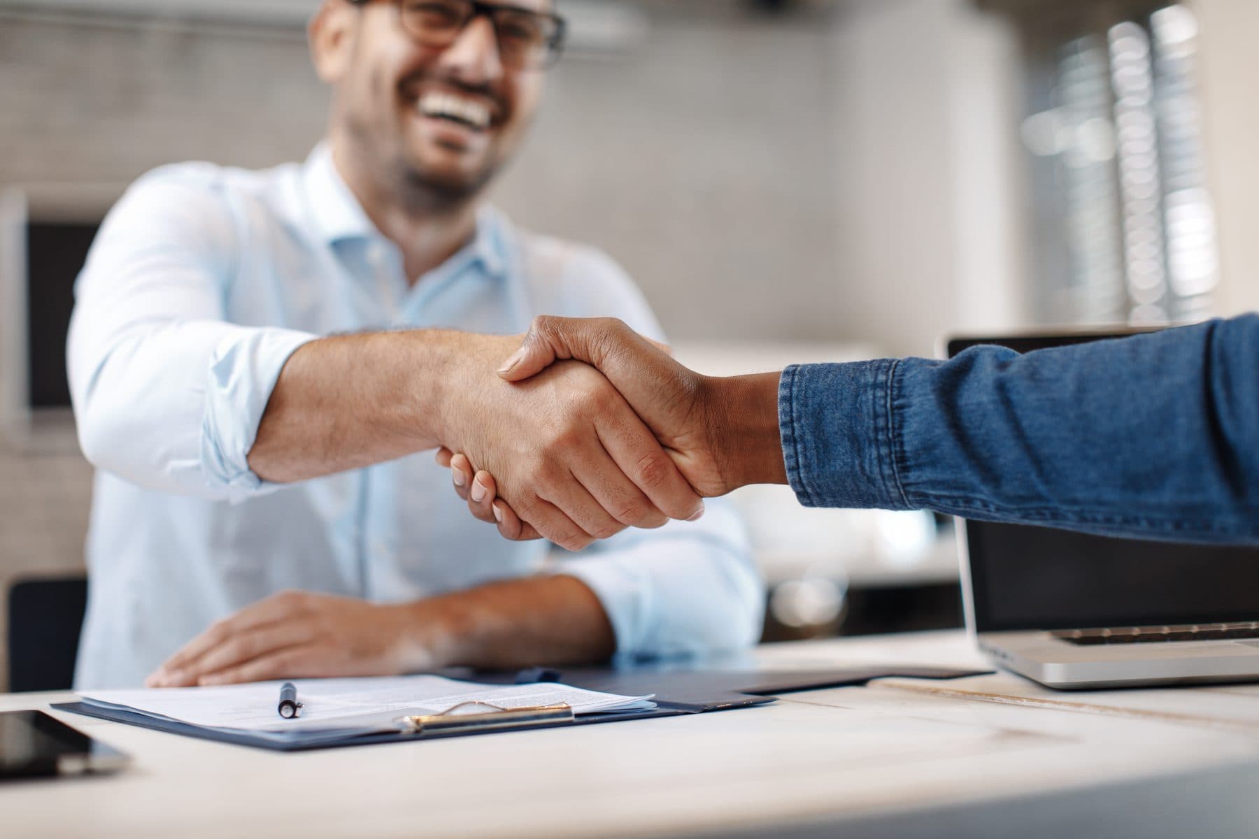 Two people shaking hands across a desk after signing an agreement