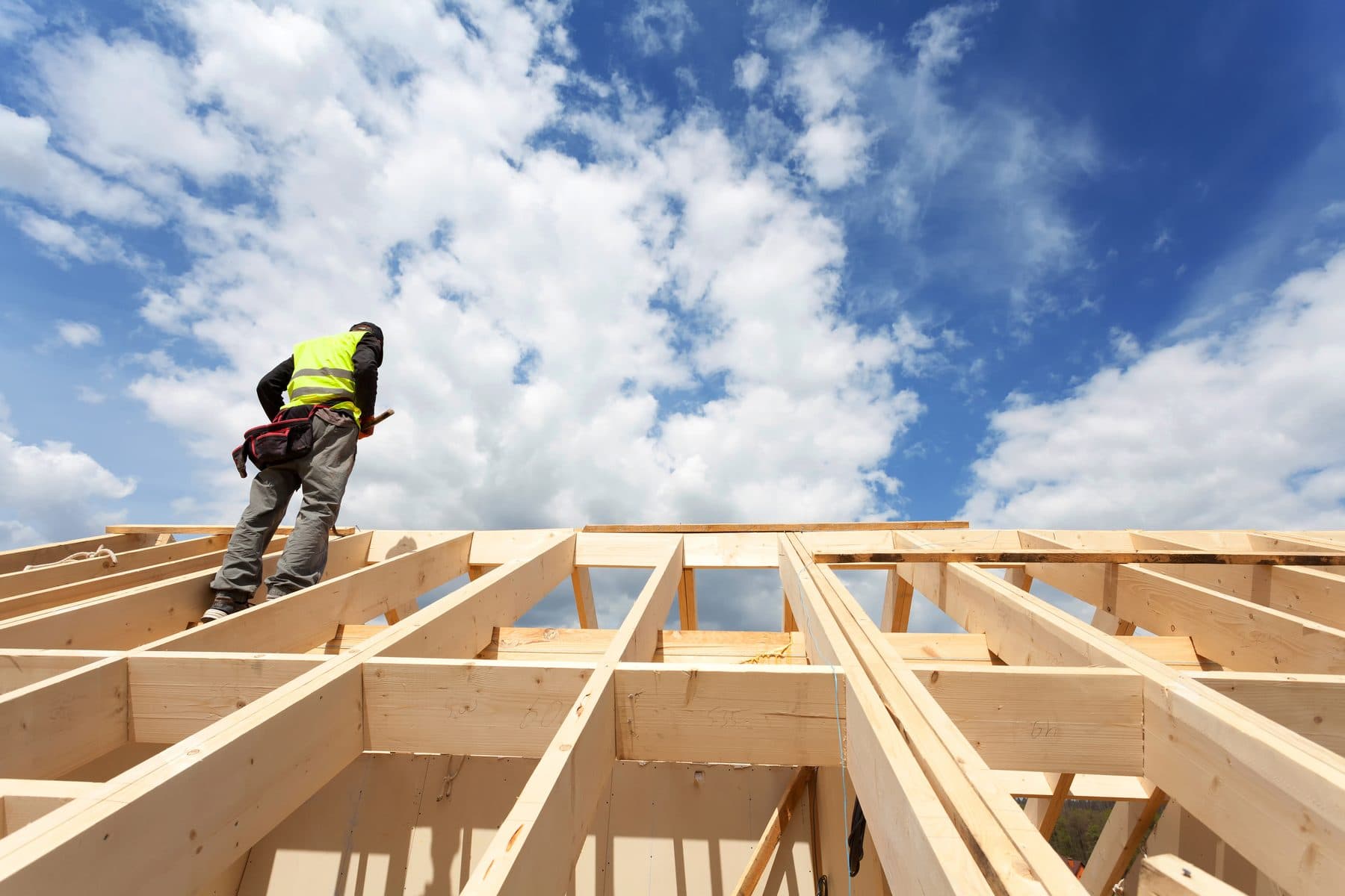 A crew member in a high-visibility vest working on a timber roof frame against a blue sky